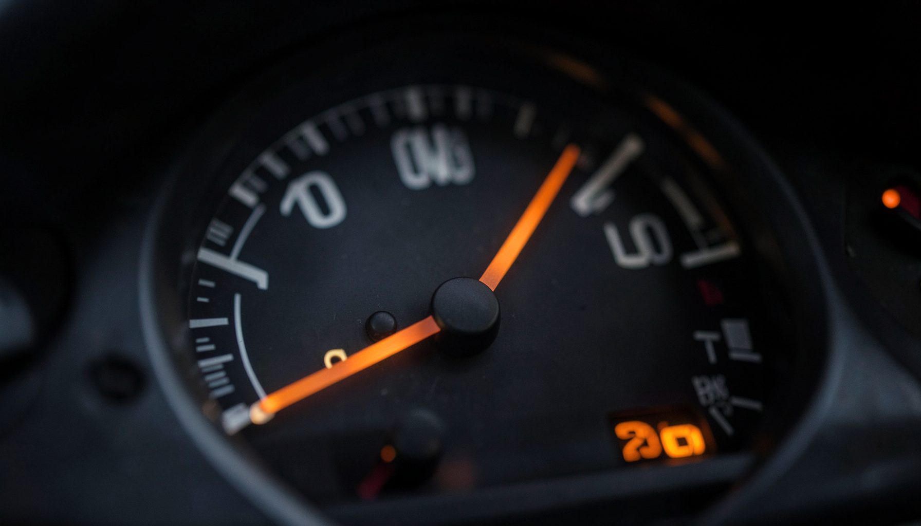 A close-up of a fuel gauge needle approaching empty with soft dashboard lighting, evoking the importance of fuel economy
